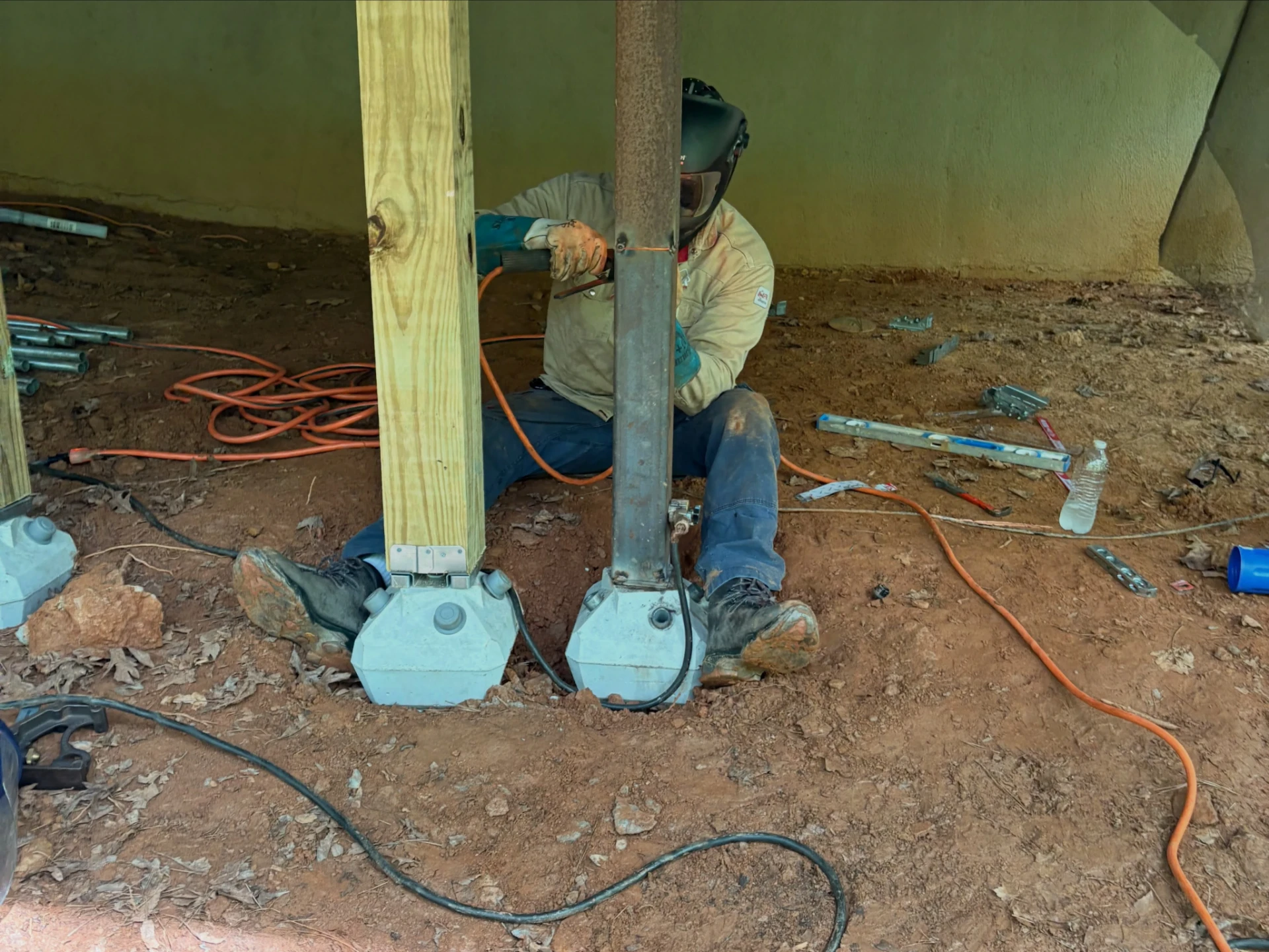 Welder working beside a replacement steel deck support mounted on a concrete footing between wooden posts