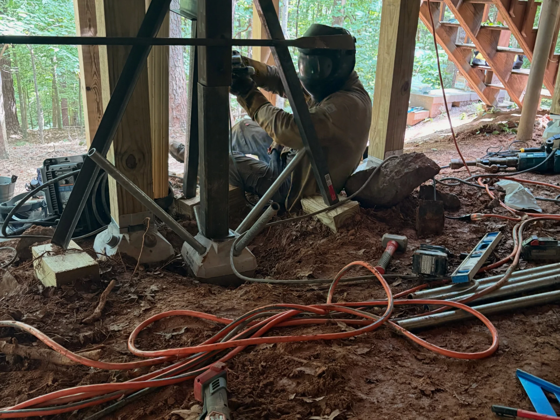 Welder positioning equipment beside a steel deck support with welding leads across the ground