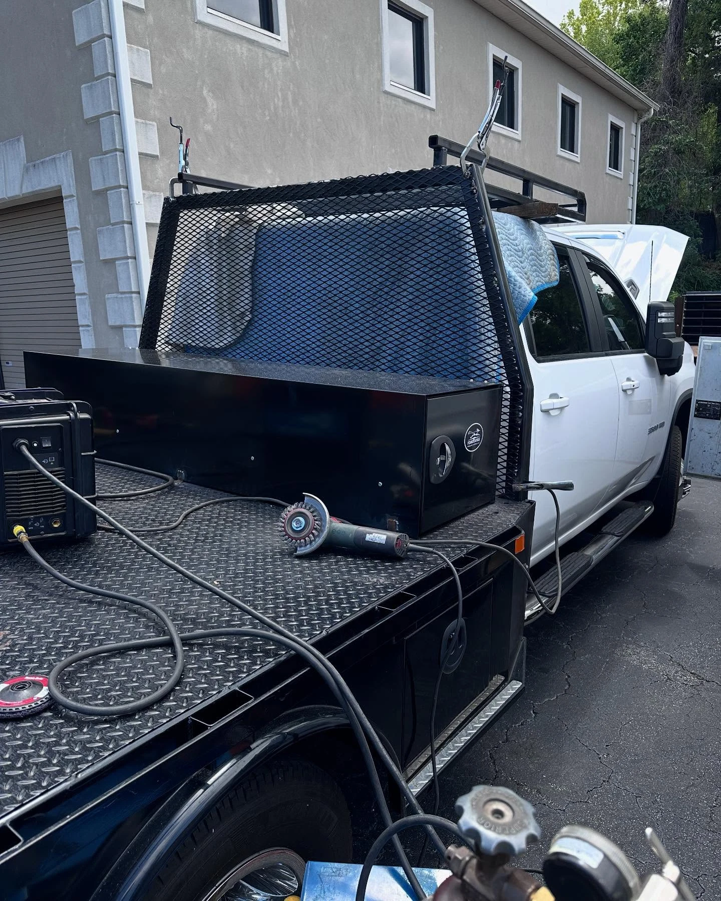 White flatbed welding truck with custom mesh cab guard, over cab rack and black storage boxes along the bed