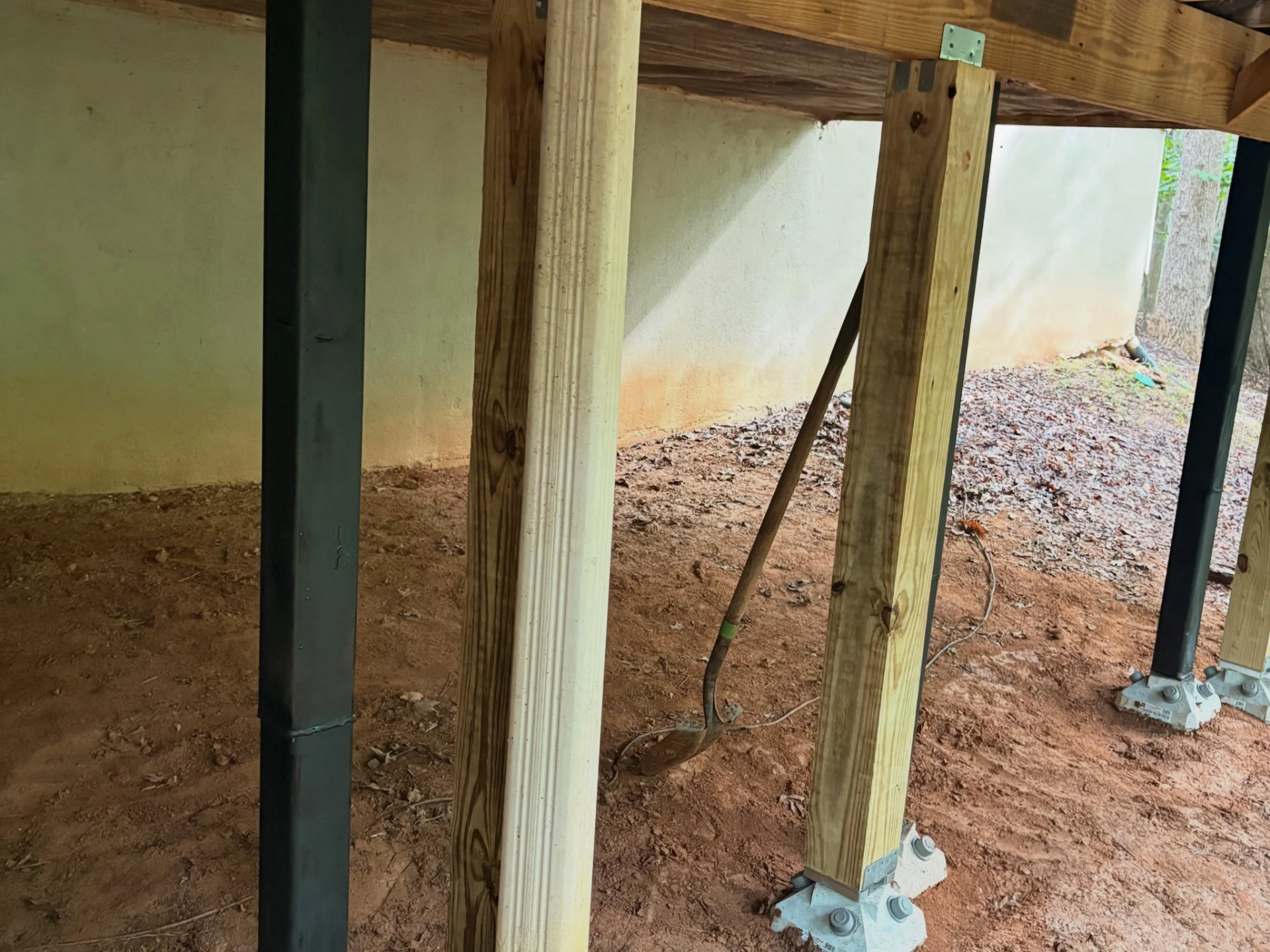 Steel deck support post fitted beside wooden posts beneath the deck framing