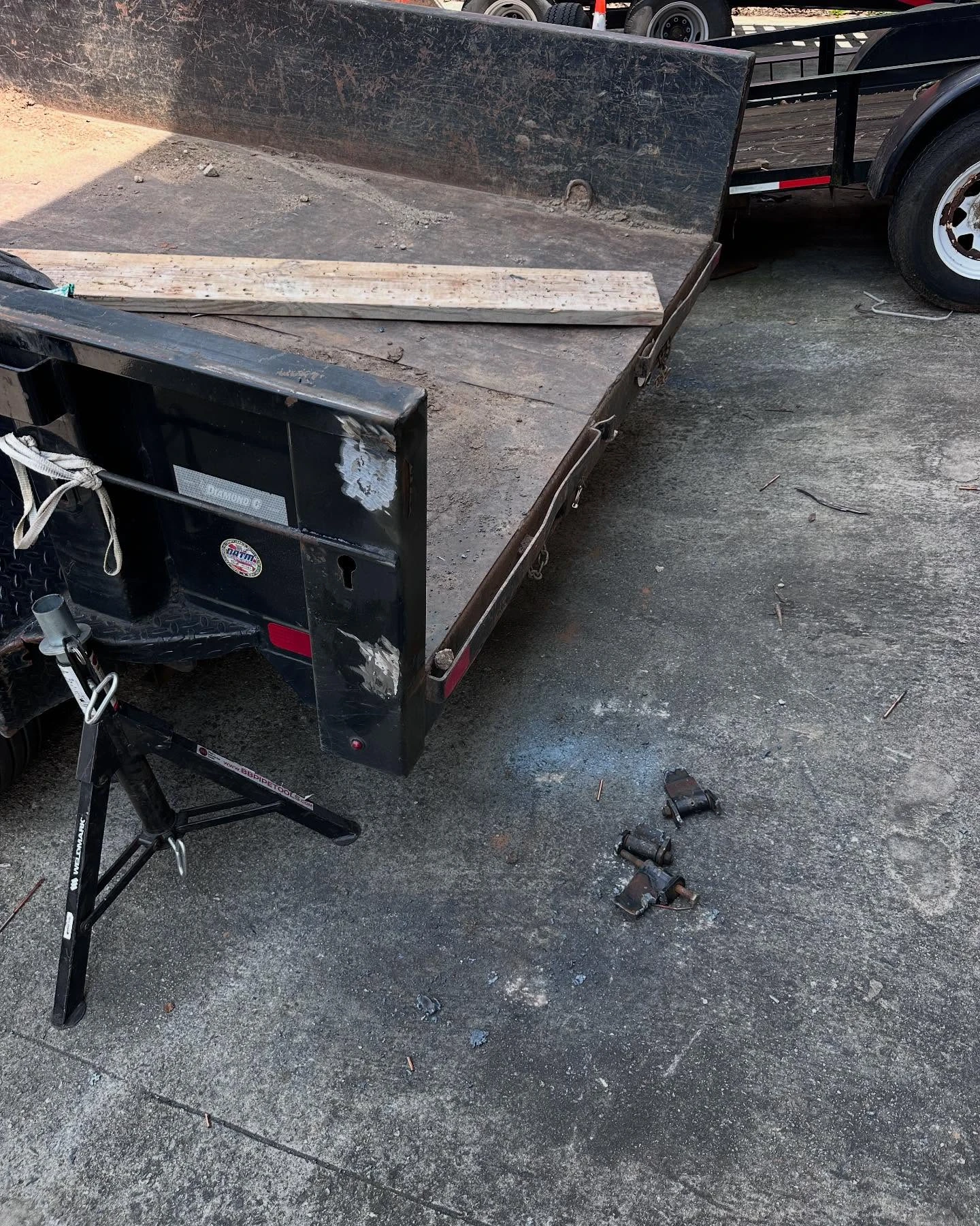 Dump trailer raised on jack stands with removed hydraulic cylinder parts on the ground during repair