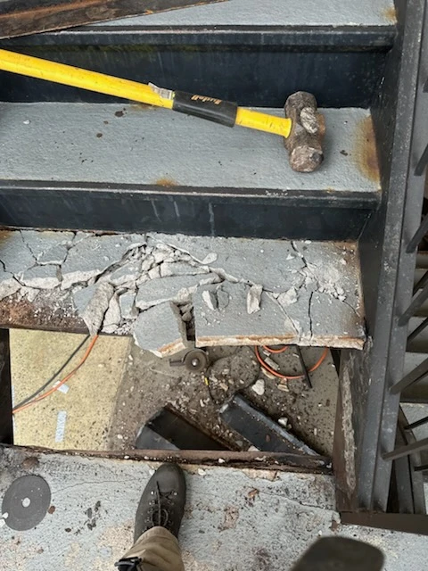 Broken concrete stair tread in a steel pan with removed debris and a hammer on the step above