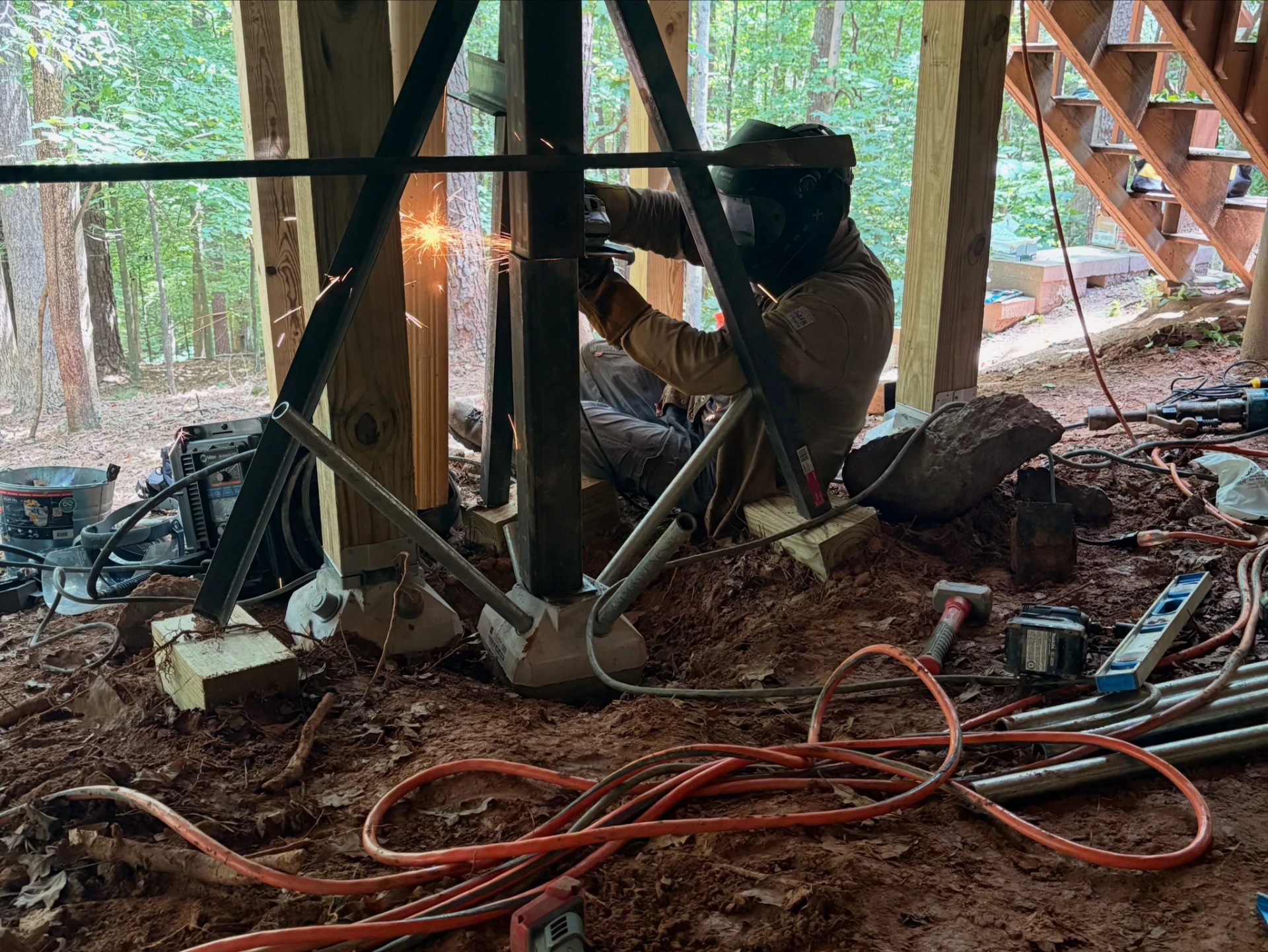 Welder working on a steel support beneath a raised deck with sparks visible at the weld