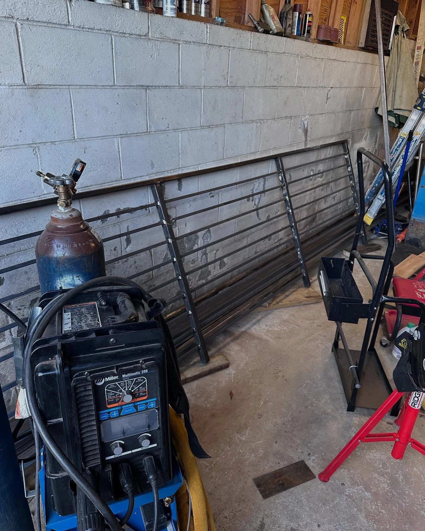 Welding machine and gas cylinder beside steel railing panels in an enclosed work area
