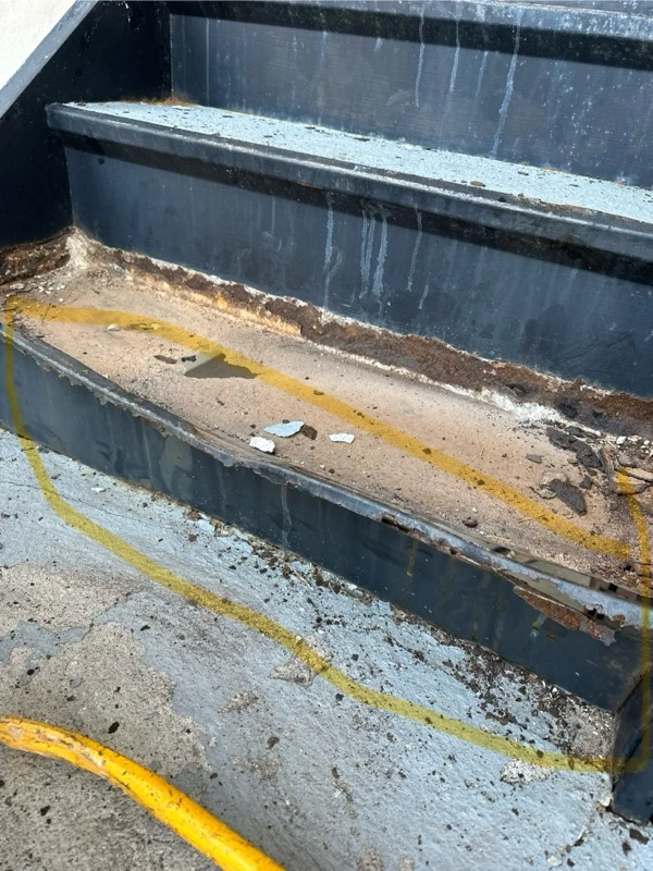 Open steel stair tread pan showing rust and remaining debris before repair